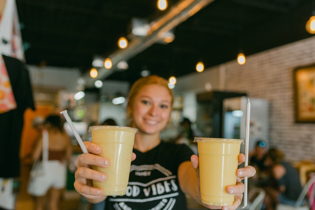 woman serving two smoothies across a counter with a bright smile in Good Vibes Cafe in Lake Placid, Florida