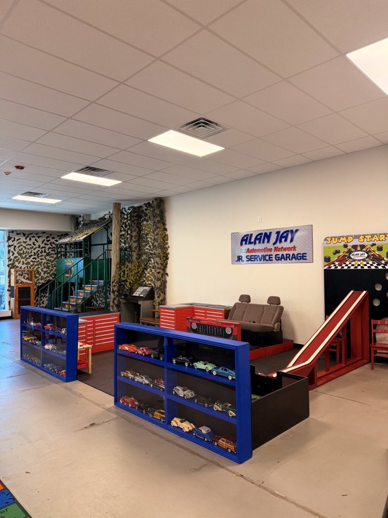 In the background their is a camo background with a child's fort and in the forefront there is a mock up of a service garage, blue shelves in the front and a mini race track on the right hand side.