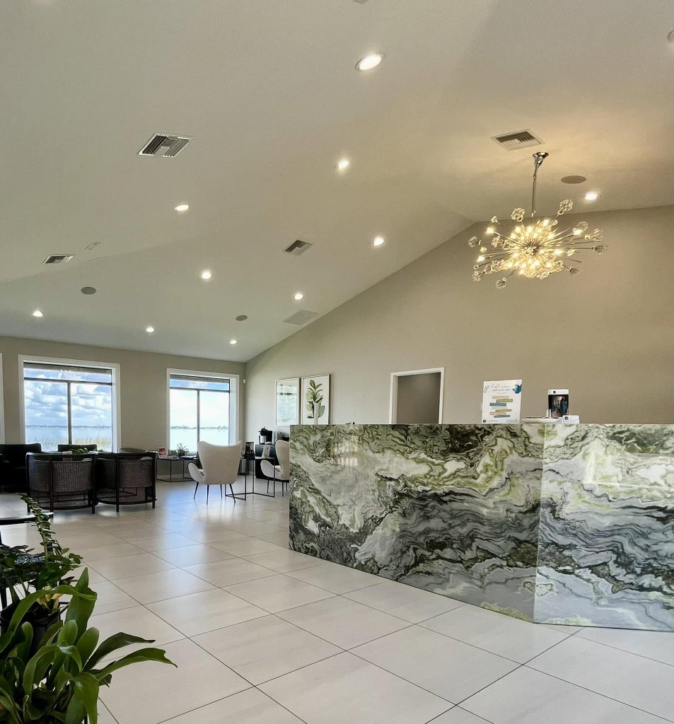 Interior of Florida Lakes Spa in Sebring, featuring a green marble reception desk, modern chandelier, seating area, and large windows overlooking Lake Jackson