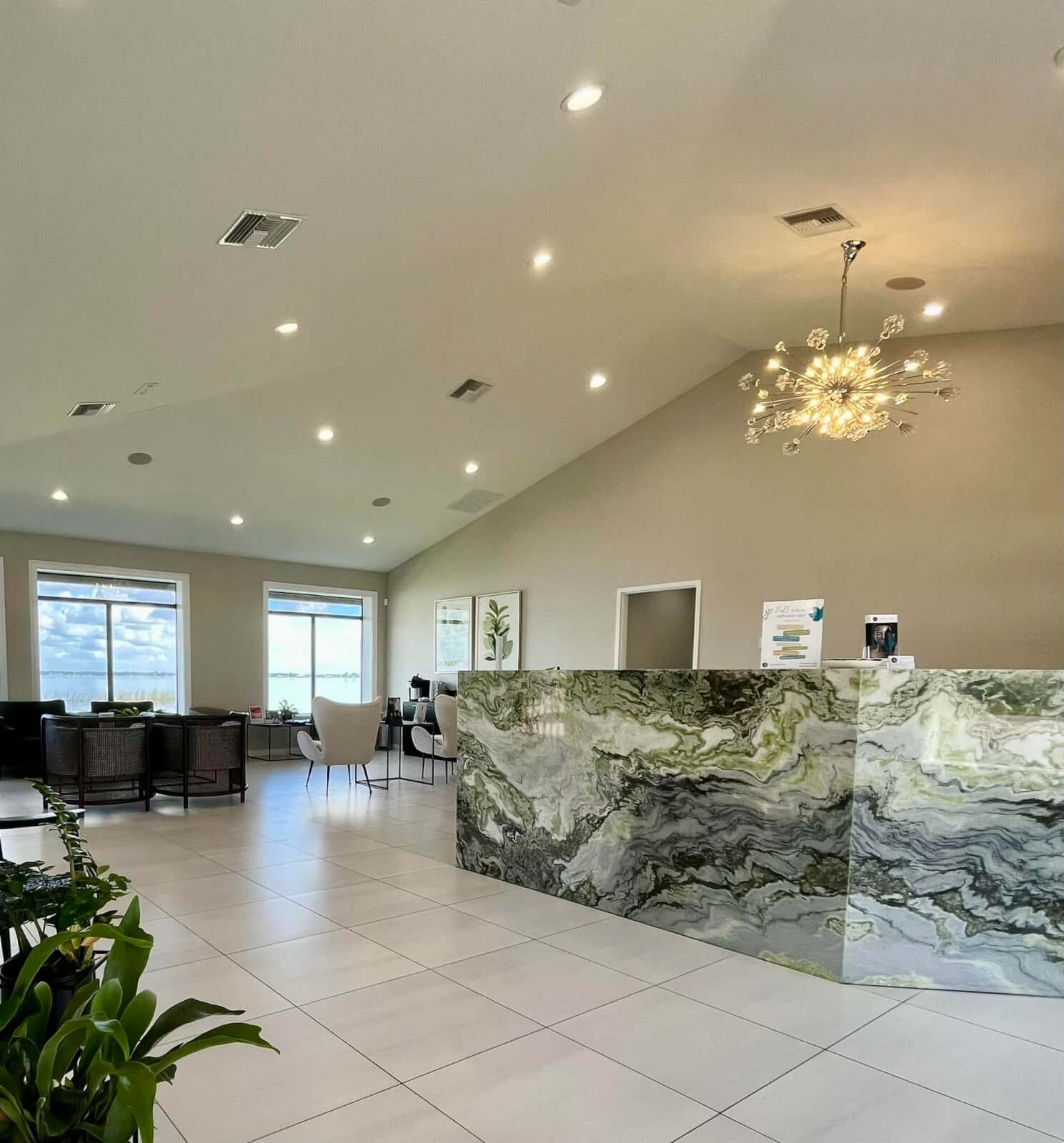 Interior of Florida Lakes Spa in Sebring, featuring a green marble reception desk, modern chandelier, seating area, and large windows overlooking Lake Jackson
