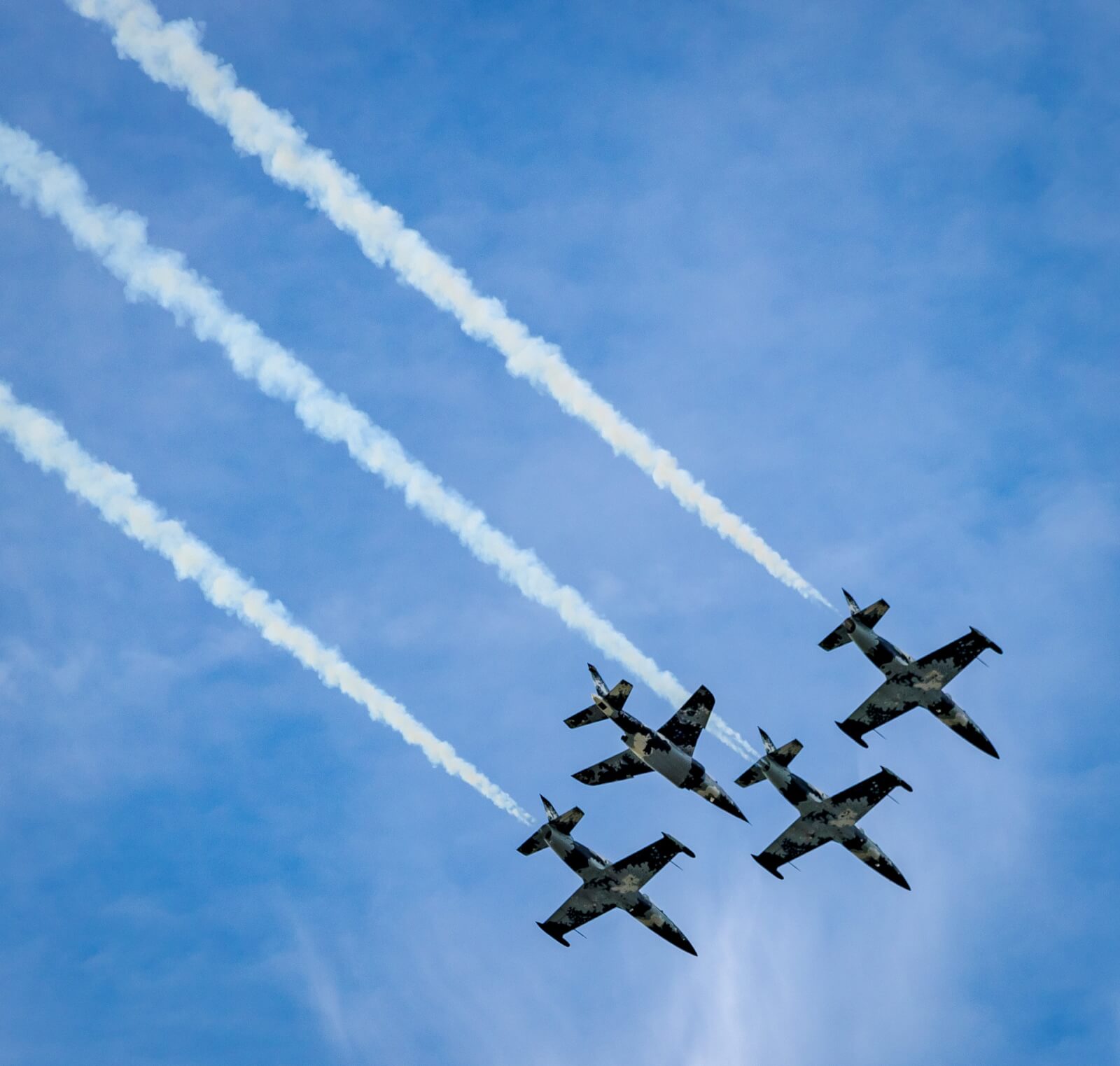 Four aircraft fly in formation with white smoke trails against a blue sky above Sebring International Raceway.