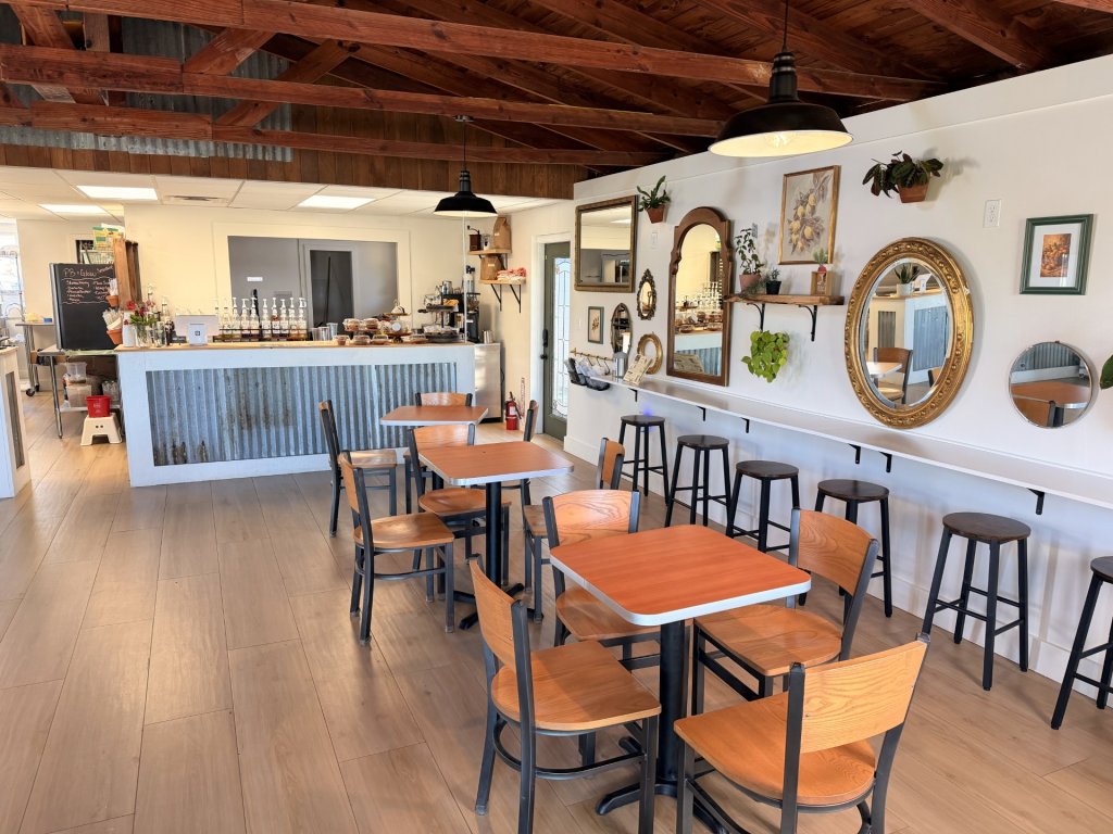 GHCCC-visit-sebring-fl Inside eating space of Grove House collective. Dark brown beams in the ceiling, wooden tables and chairs, and a wall decorated with an array of mirrors and frames.