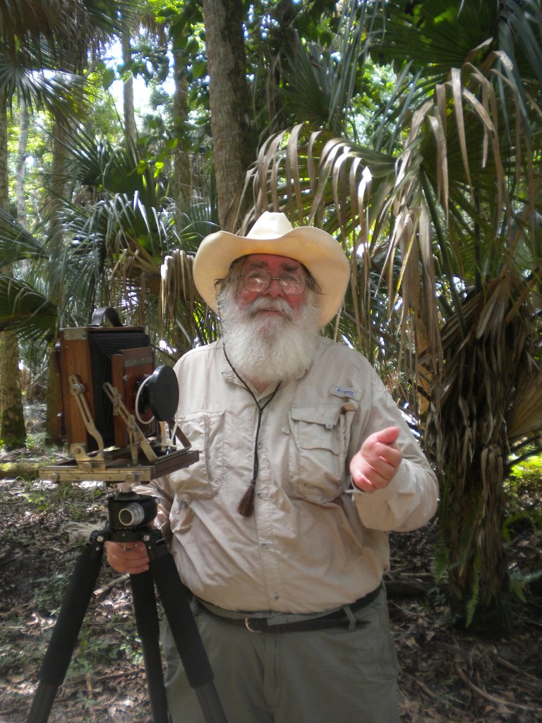Older gentleman with an old fashioned camera standing in front of Highlands Hammock foliage.