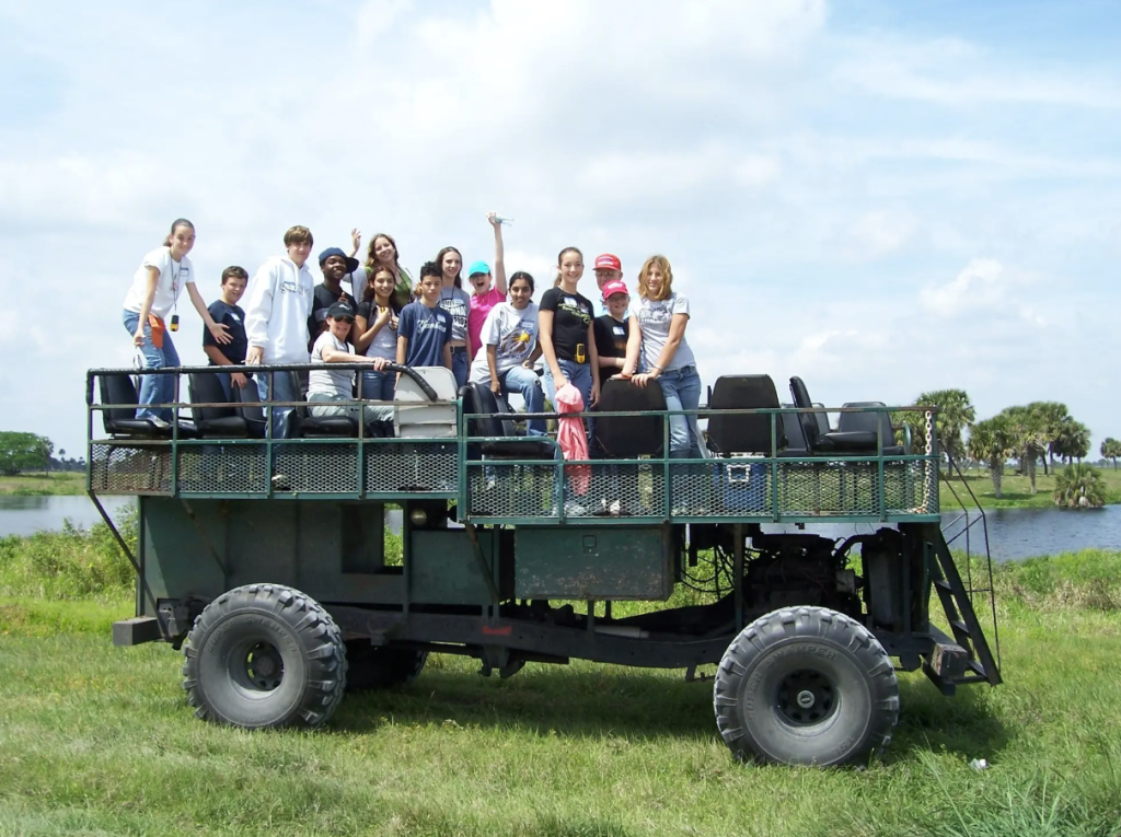 Group of 15 children and adults posing atop a large swamp buggy as part of a tour at Archbold Biological Station in Venus, FL