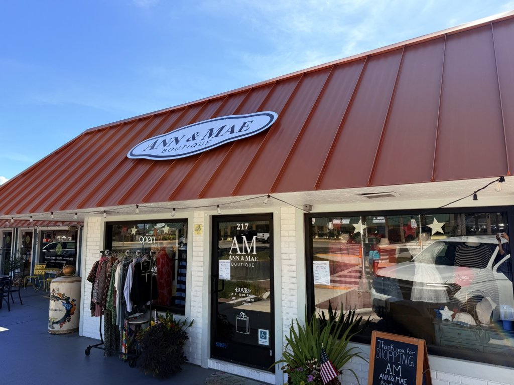 ann-visit-sebring-fl Outside storefront of Ann & Mae Boutique, brick colored roof, big open storefront windows with a rack of clothes from the boutique outside.