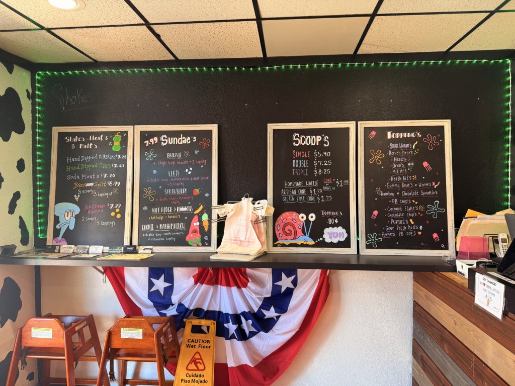 Black boards displaying menu written on with colorful writing against a black painted wall and black and white ceiling