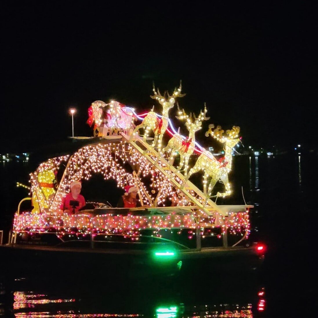 Nighttime Christmas parade boat on Lake Jackson in Sebring, Florida, adorned with bright holiday lights, reindeer figures, and festive riders.
