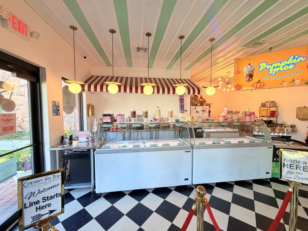 Warmly lit interior of an ice cream shop featuring black-and-white checkered floors, a mint and white striped ceiling, and a glass display case showcasing a variety of ice cream flavors.