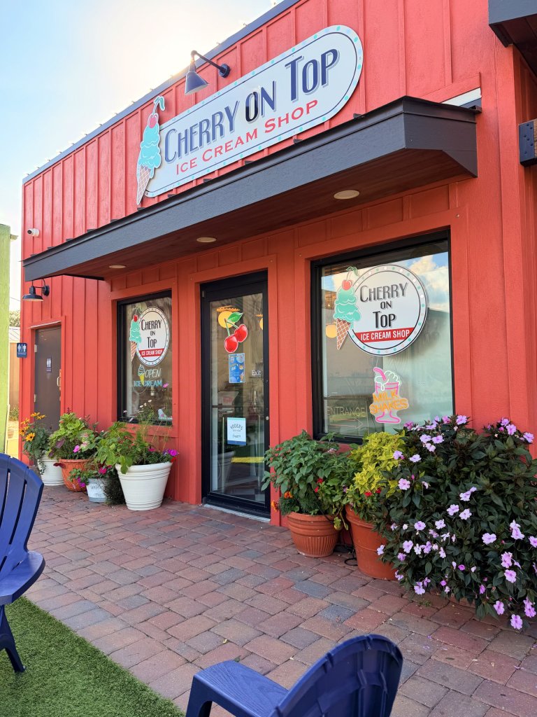 Red wooden exterior of an ice cream shop in Lake Placid, Florida, featuring ice cream cone decals and business logos on the windows, door, and signage.