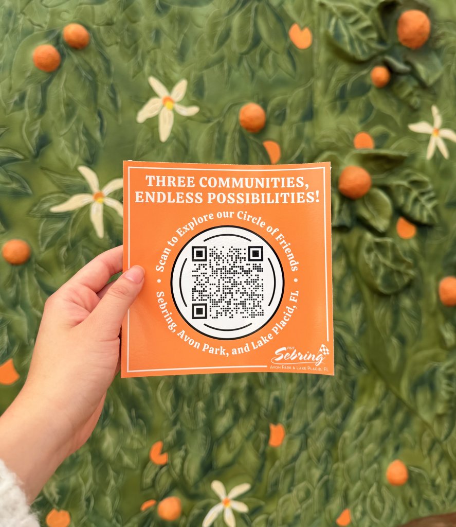 Hand holding orange QR sticker against green mural with painted oranges
