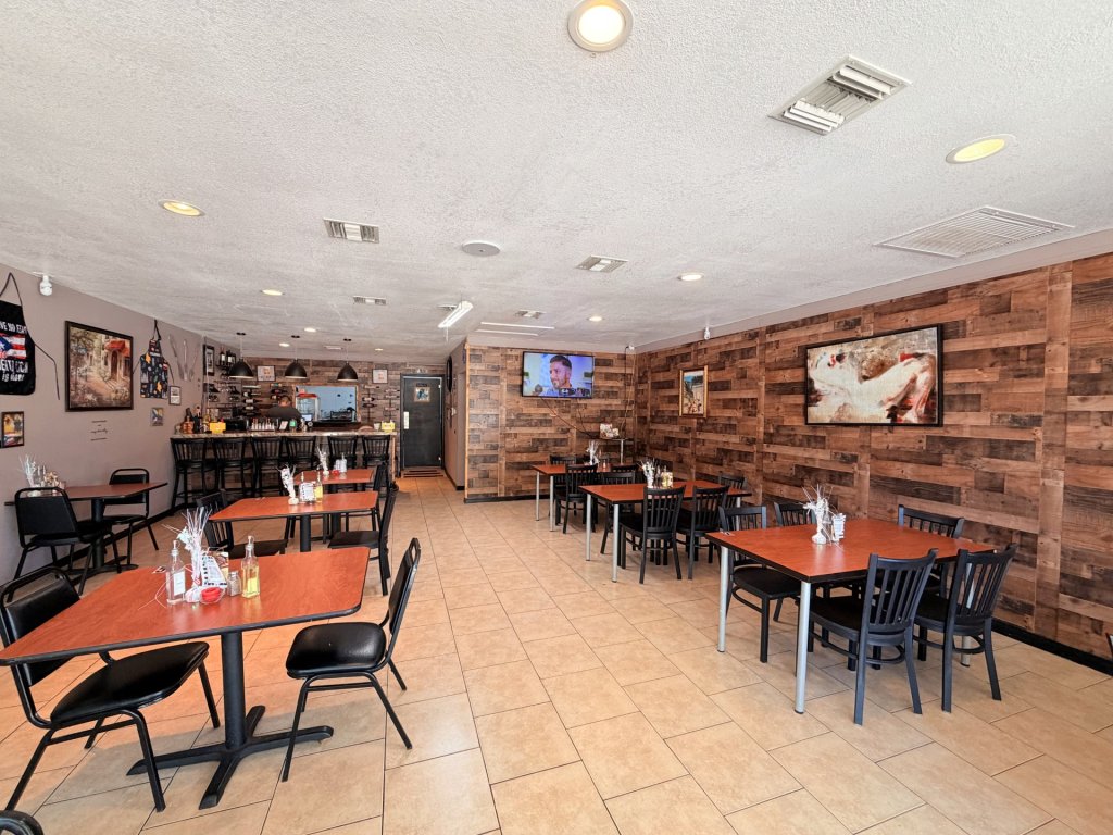 Restaurant interior showing tiled flooring, large tvs on walls, tables laid out, and a bar towards the back.