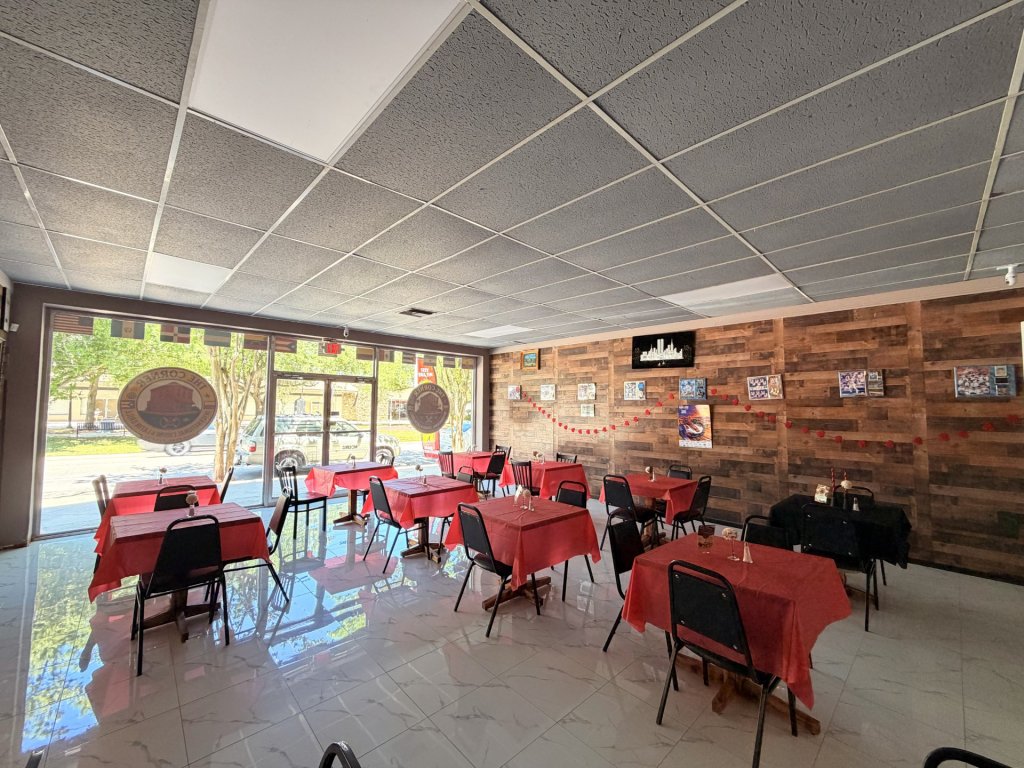 Further interior of the restaurant, with scattered tables and chairs for dine in seating decorated with red table cloths.
