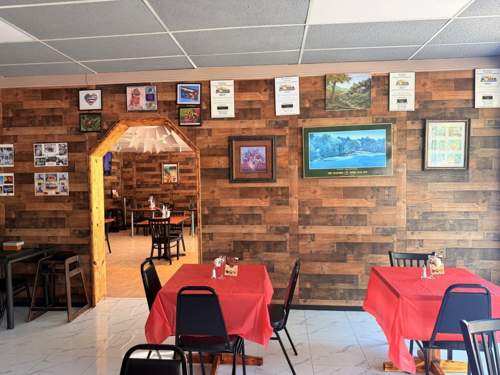 Wall of interior showing archway that connects both sides of restaurant. A wooden wall with multiple frames displayed.