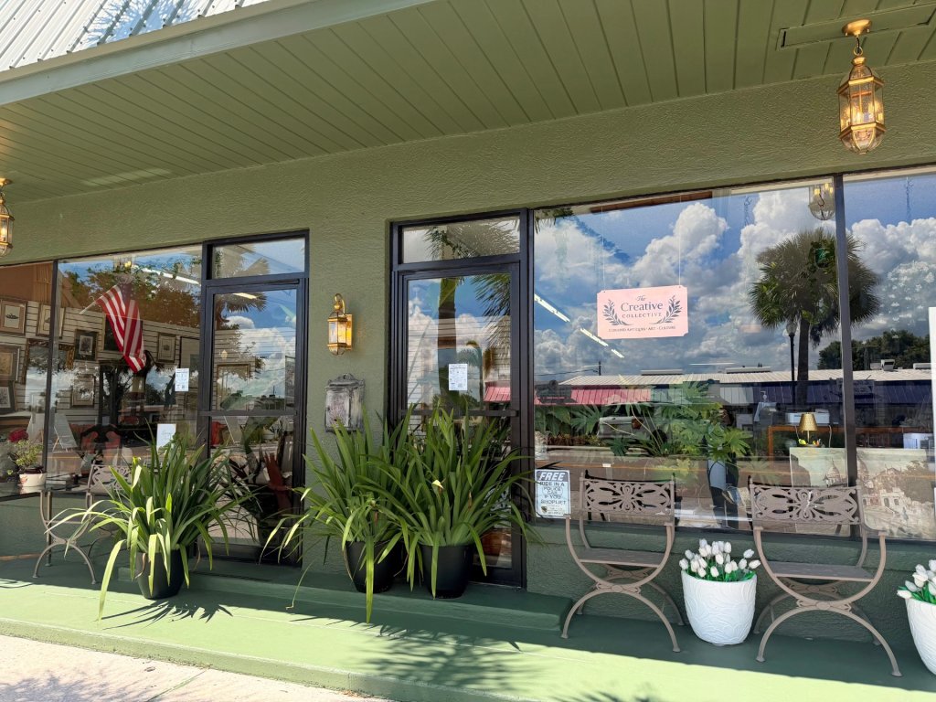 Outside exterior of storefront, featuring a green painted storefront and plants outside lining the large display windows