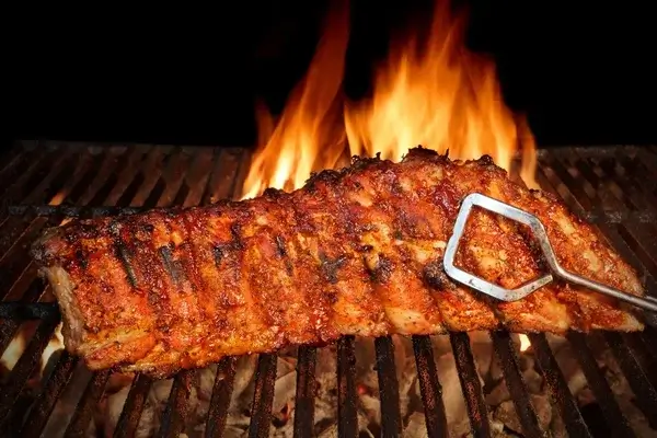 baby back ribs held in tongs on a grill with open flame behind