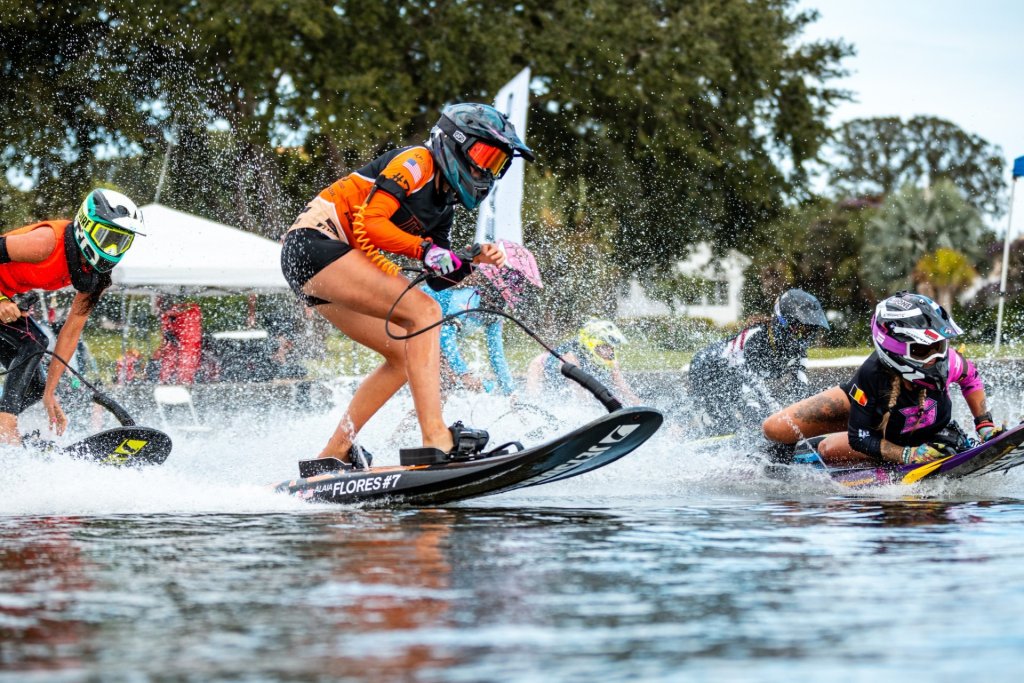Professional athlete in orange athletic swim wear on a motorized surfboard in a competition in the water with other racers.