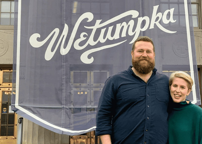 Couple stands in front of building that displays a large We Love Wetumpka banner