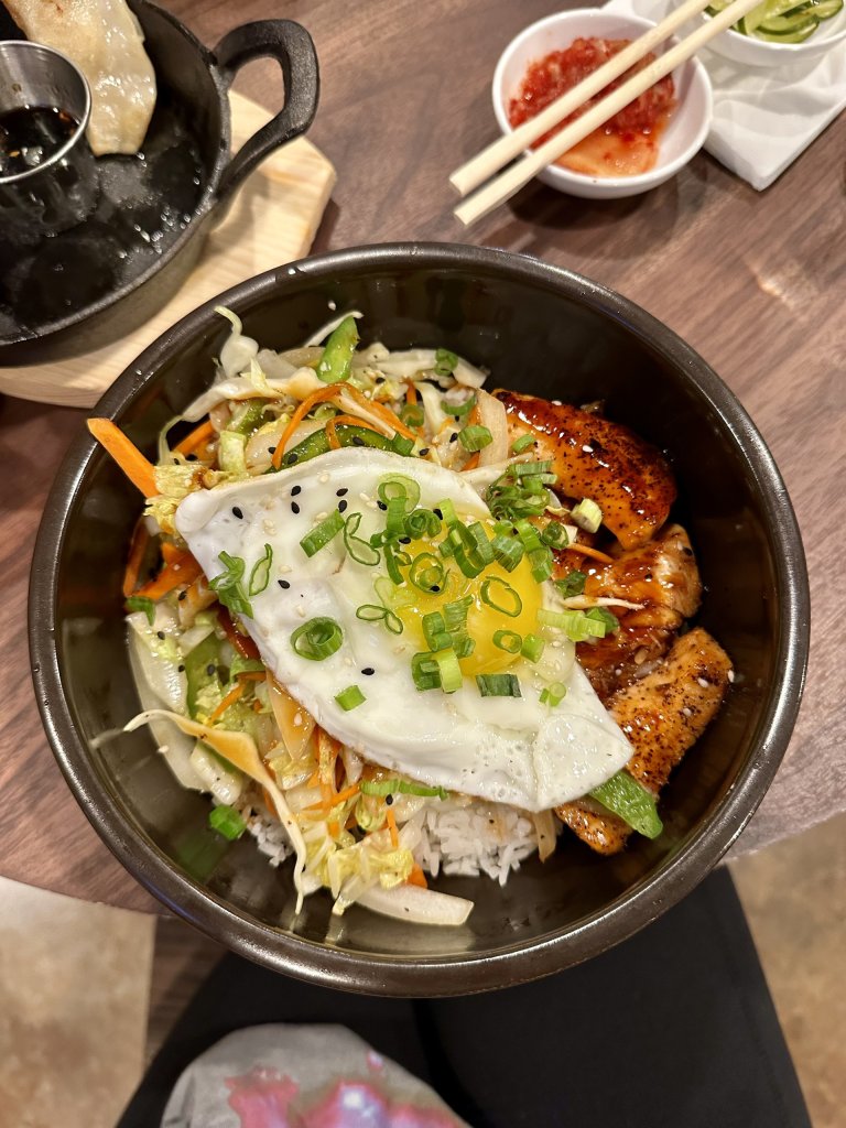 Hot stone bowl from Jinsoo Kitchen in Sebring, Florida with a bed of rice, fresh salmon, a soft-cooked egg on top, and chopped scallions, showcasing authentic Asian fusion cuisine.