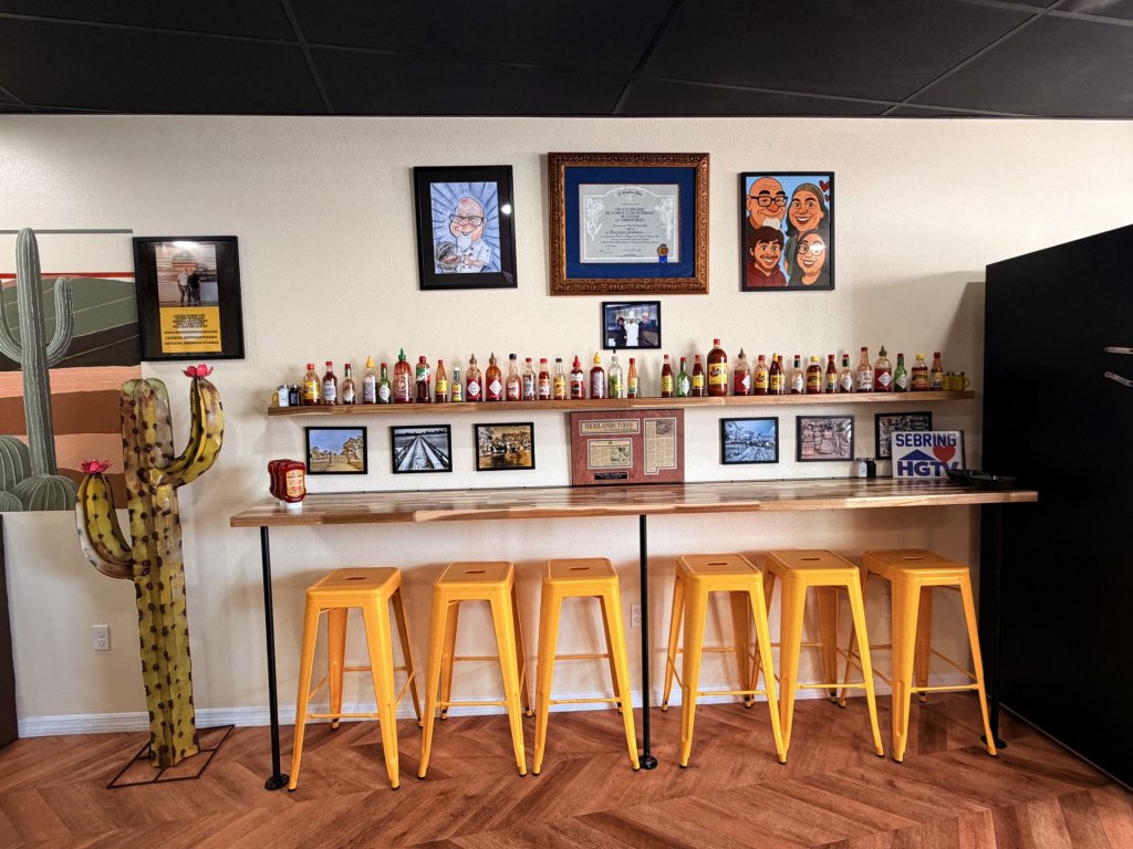 "Wall of hot sauces" Indoor bar stool seating on yellow bar stools. Faux cacti decor and a long row of different types of hot sauces that can be used on meals purchased there.
