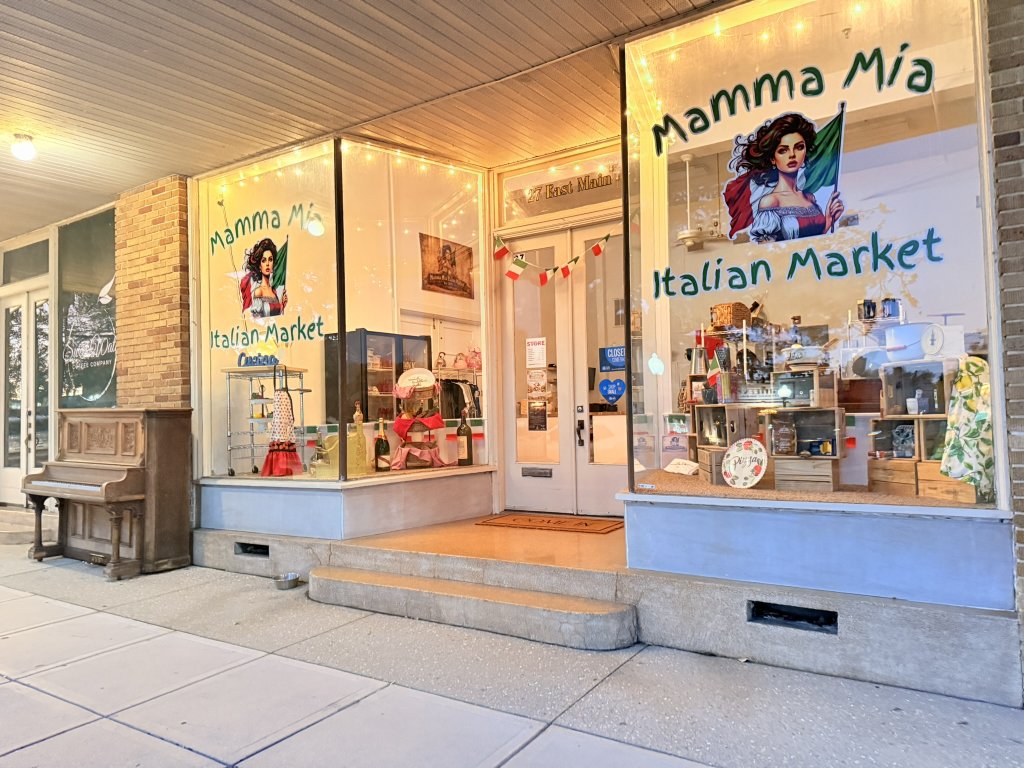 Outside storefront with big windows looking into the Italian market. Glowing border lights illuminate the entrance.