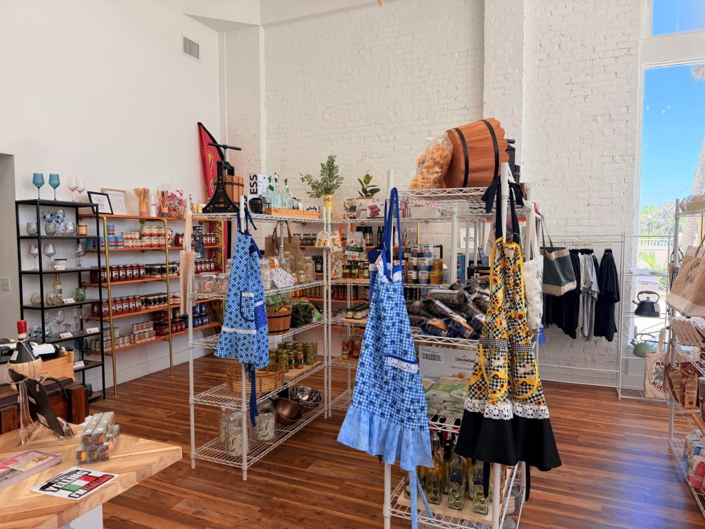Inside view of Italian market, metal shelves displaying food items, colorful aprons, other food goods.