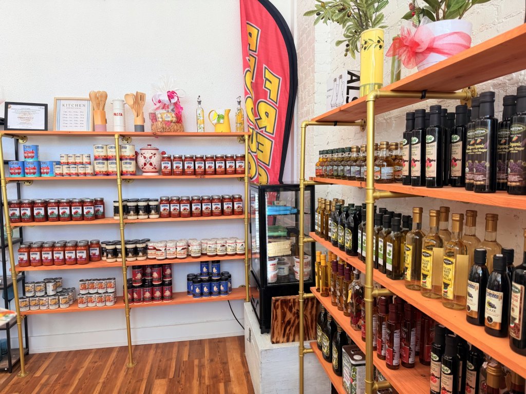 Shelves displaying food goods such as olive oil, balsamic vinegar, white cooking wine, and a variety of sauces.