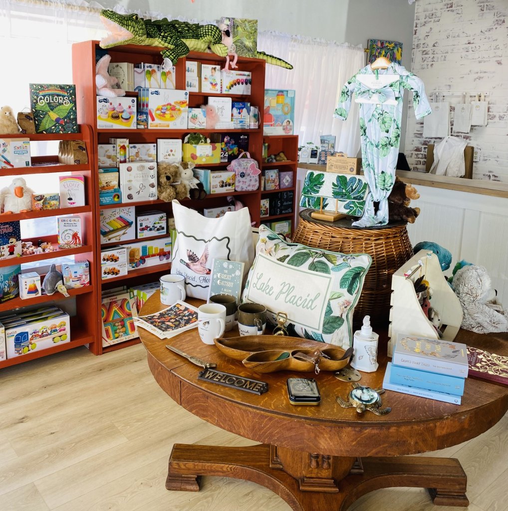 mudddd-visit-sebring-fl Boutique interior showing a shelf filled with a variety of children’s toys and a table display featuring Lake Placid memorabilia, keepsakes, and baby clothes arranged for shoppers.