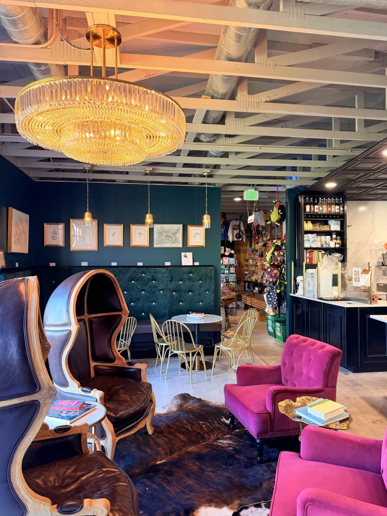 owll-visit-sebring-fl Warm, inviting café interior featuring a glowing crystal chandelier, emerald tufted wall seating, gold café chairs, magenta armchairs, and unique dome-back leather chairs arranged around a cowhide rug.