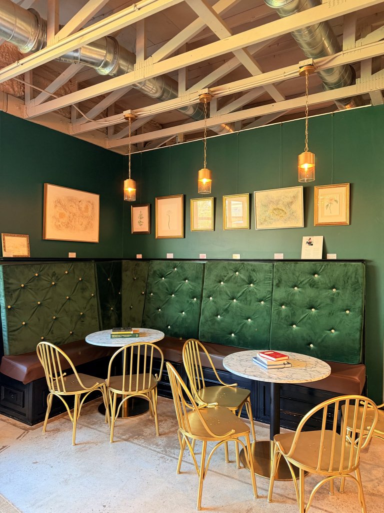 owlll-visit-sebring-fl Emerald tufted wall seating, gold café chairs, marble coffee tables, and gold frames decorating the back walls.