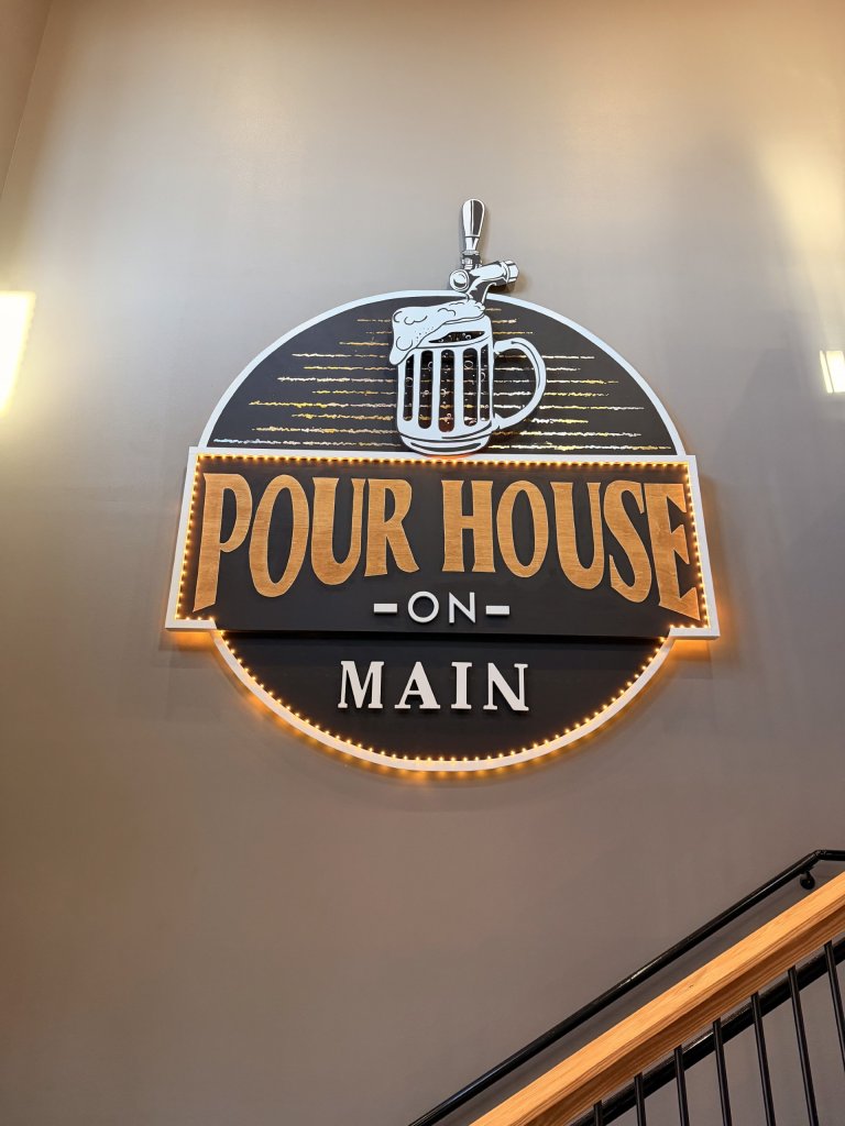 pour house-visit-sebring-fl Illuminated “Pour House on Main” brewery sign featuring a beer mug tap logo, warm LED backlighting, and modern rustic wall décor inside a craft beer bar or self-pour taproom.