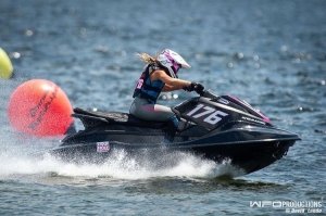 Woman decked in helmet and life jacket leaves a trail of water spray behind as she races jet ski on Lake Jackson in Sebring Florida as part of the area's annual Pro Watercross event