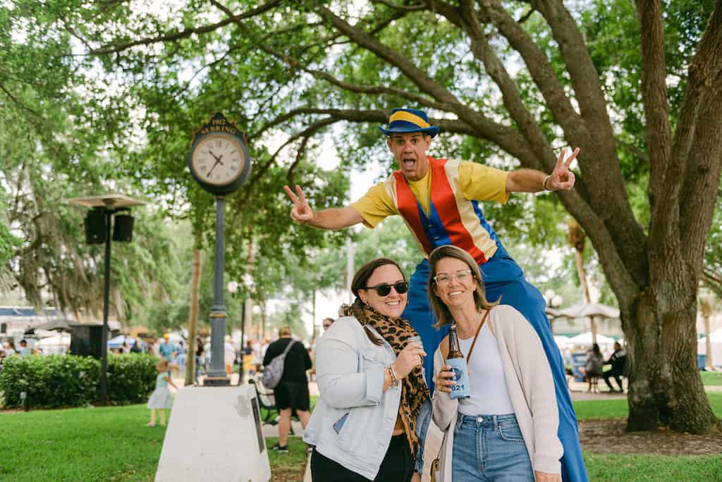 two women enjoying craft sodas pose with man on stilts at Sebring's Soda Festival