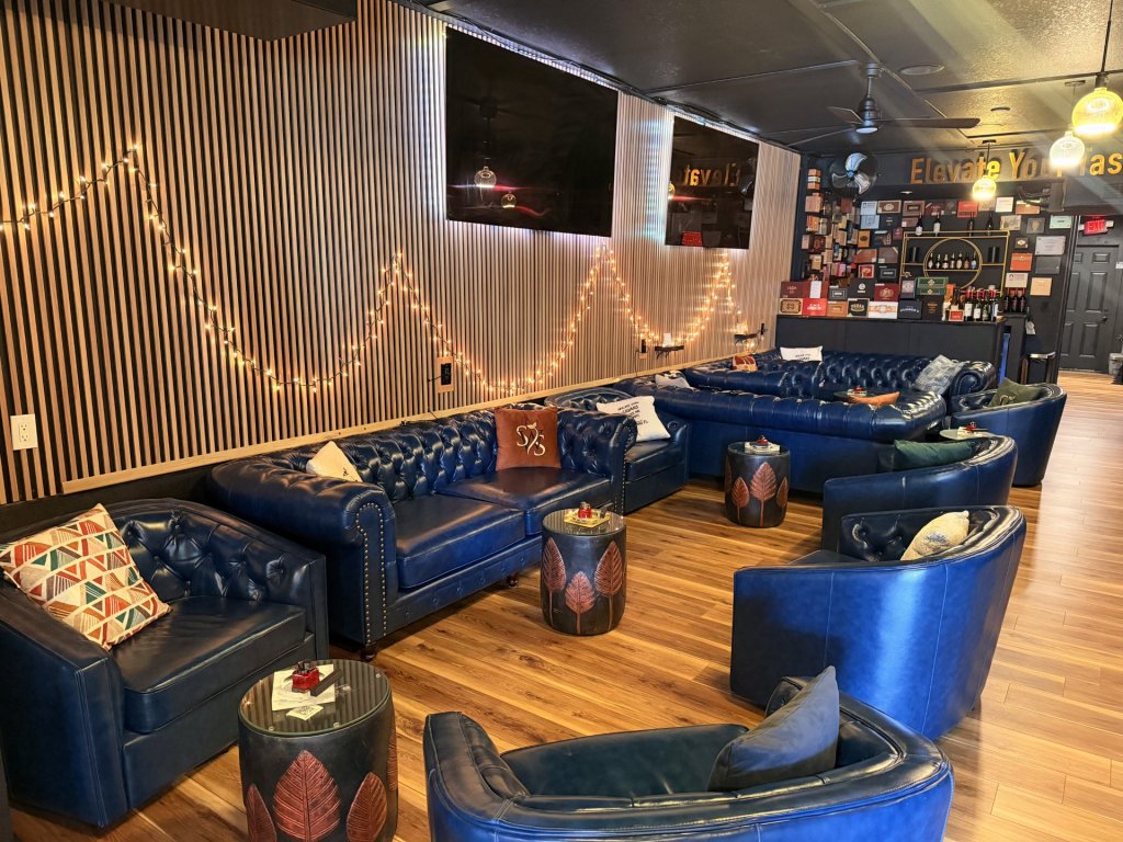 Cozy interior of a Sebring, Florida cigar lounge with blue leather Winchester chairs and couches arranged against a rich wooden wall, creating a warm and inviting atmosphere.