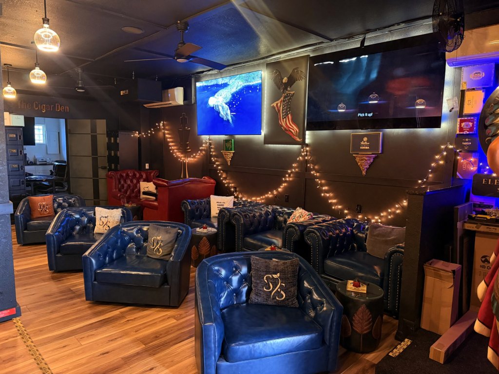 Cozy interior of a Sebring, Florida cigar lounge with blue leather Winchester chairs and couches arranged against a rich wooden wall, creating a warm and inviting atmosphere.