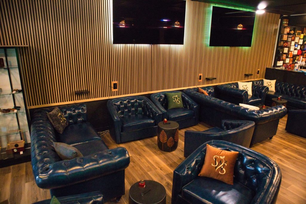 Cozy interior of a Sebring, Florida cigar lounge with blue leather Winchester chairs and couches arranged against a rich wooden wall, creating a warm and inviting atmosphere.