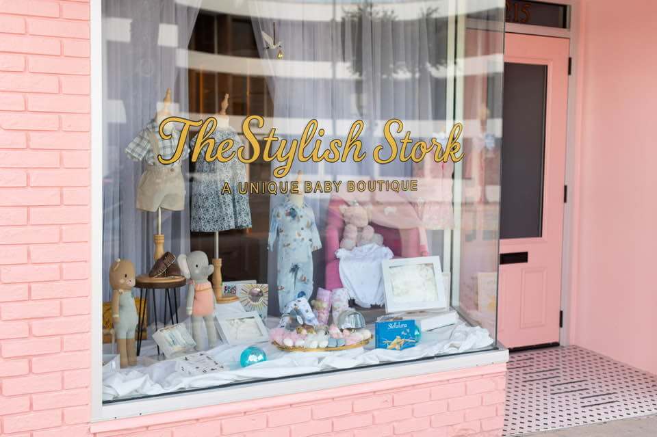 Storefront of The Stylish Stork baby boutique in Sebring, FL, featuring pastel pink exterior, curated baby clothing, toys, and gifts displayed in the window.