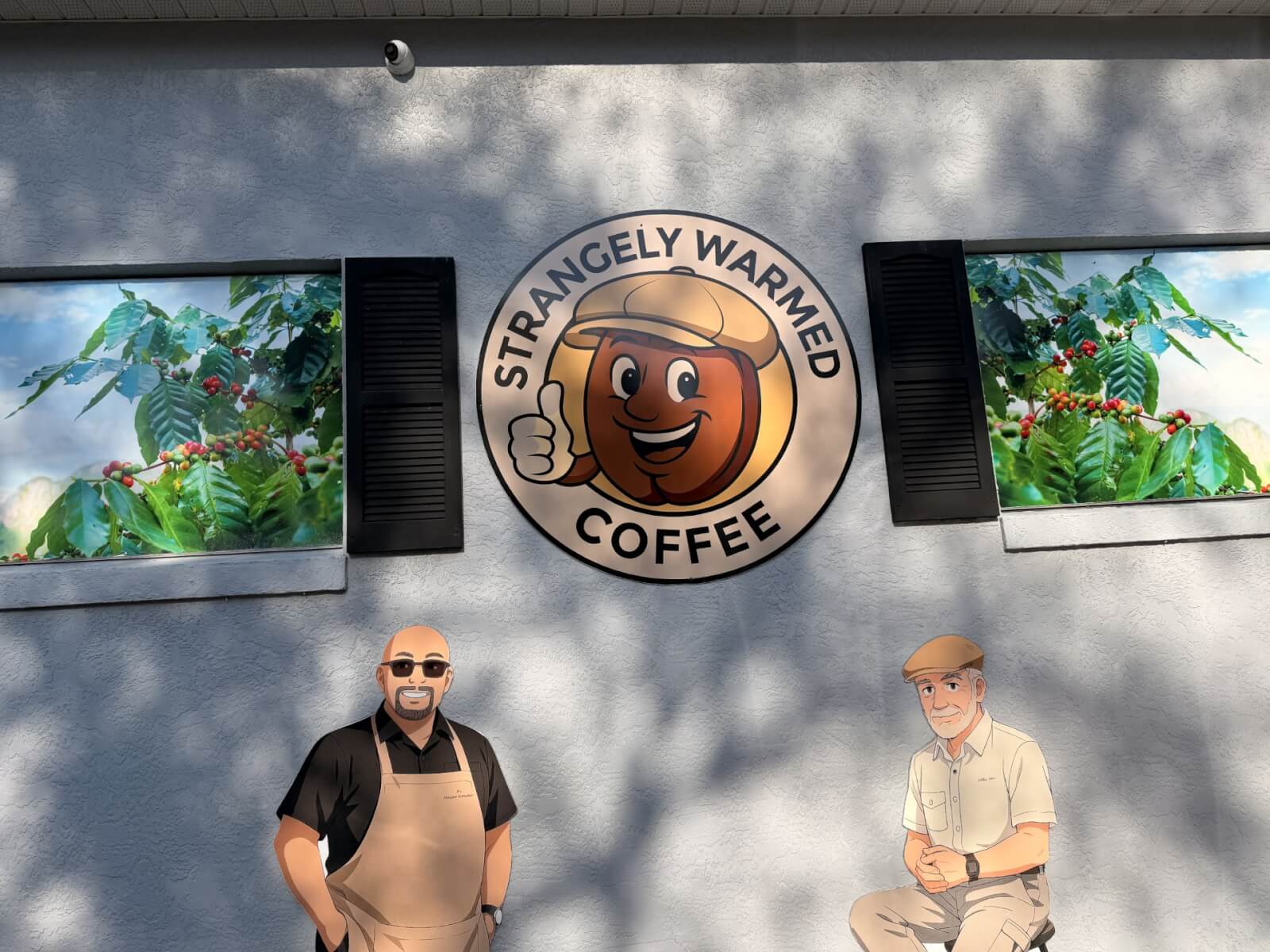 strangely-visit-sebring-fl Exterior wall of Strangely Warmed Coffee displaying a round logo with a cheerful cartoon coffee cup. The wall features two large panels showing lush coffee plants with red cherries, framed by black shutters. Below the logo are two illustrated characters—one in an apron and sunglasses, the other seated and wearing a cap—set against a sunlit gray textured wall.