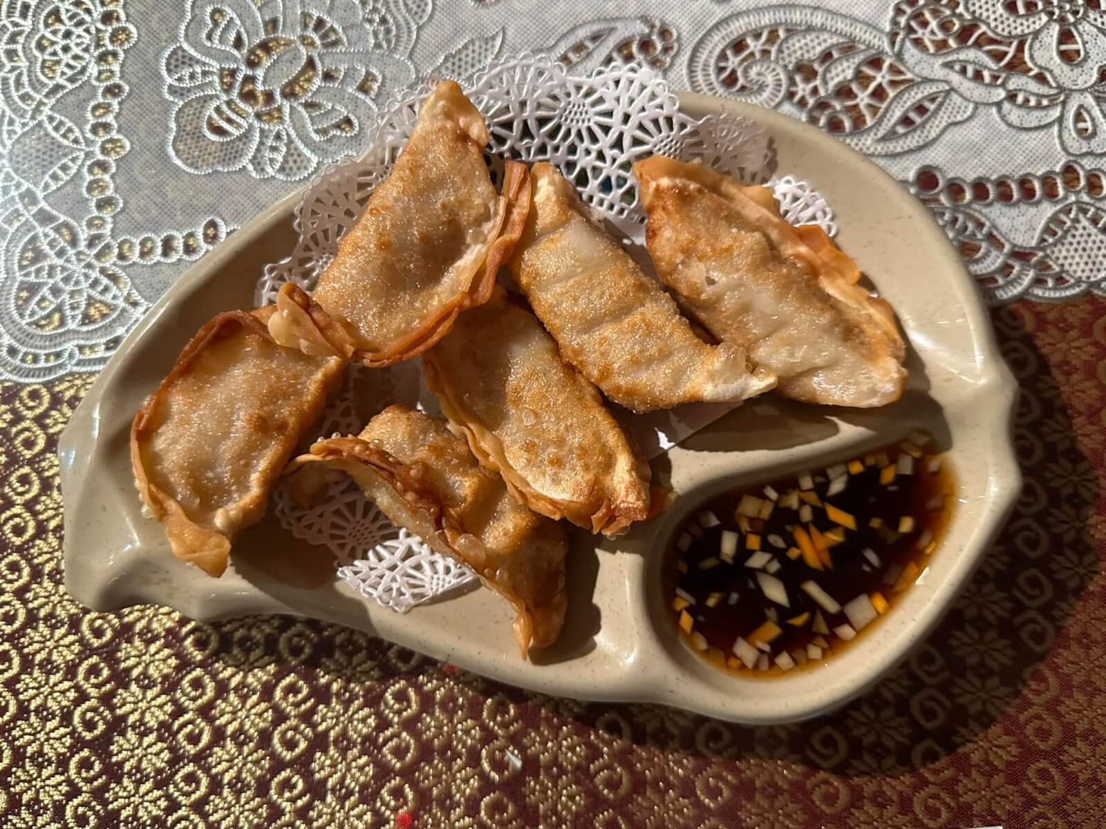 Six fried dumplings in a decorative plate served with a dark brown sauced with finely chopped carrots.