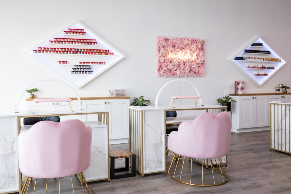 White painted nail studio in Sebring, Florida with pink accent chairs, floral portrait with neon sign and a display of all nail polishes.
